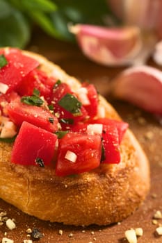 Fresh homemade crispy Italian antipasto called Bruschetta topped with tomato, garlic and basil on wooden board (Selective Focus, Focus on the tomato piece in the front) 