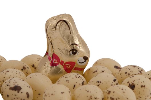 Chocolate Easter candy delicacy wrapped in foil with bunny image surrounded with small plastic eggs isolated on a white background.