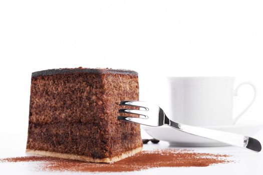 chocolate cake with a fork and a cup of coffee in background on white background