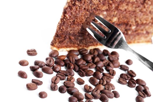 chocolate cake with a fork inside and coffee beans on white background