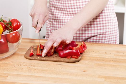closeup of hands cutting red paprika on a chopping board
