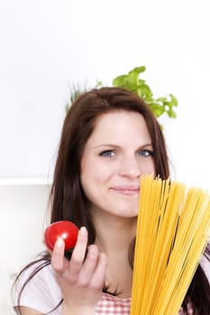 smiling young woman in a kitchen holding spaghetti and tomato