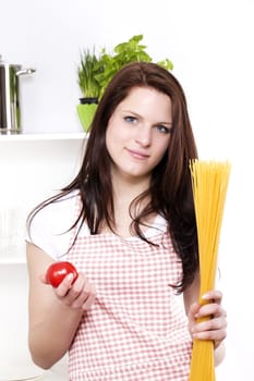 smiling young woman in a kitchen holding spaghetti and tomato