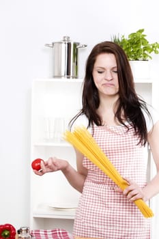 young woman holding pasta and tomato looking at the tomato in her hand