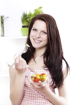 young happy woman in kitchen eating mixed salad