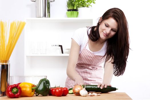 young happy woman in a small kitchen chopping cucumber for salad