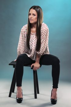 beautiful teenager sitting on a stool in blue light wearing black jeans