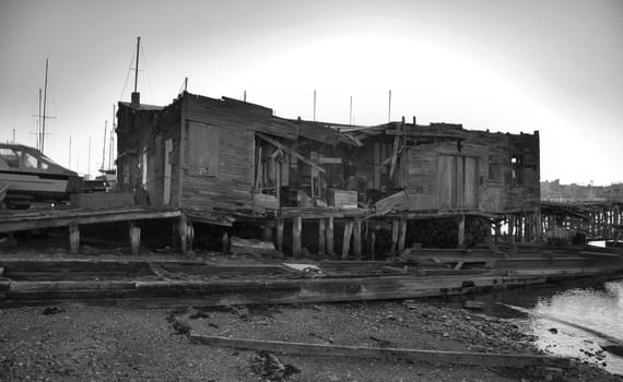 An old fallen down building along the shore. Shown in black and white.