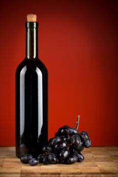 bottle of wine and grapes over red background