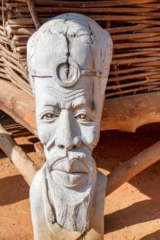 African carved wooden statue in front of dwelling