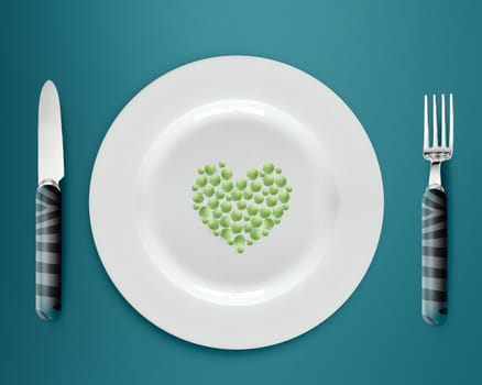 Heart shape green peas on white plate with knife and fork on blue background.