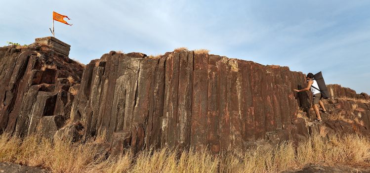 Indian man holding rocks of cliff to climb up to top flag