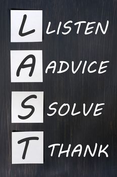 LAST (listen, advice, solve, thank) - acronym for training customer service and complaints handling. blackboard with sticky notes and white chalk handwriting 