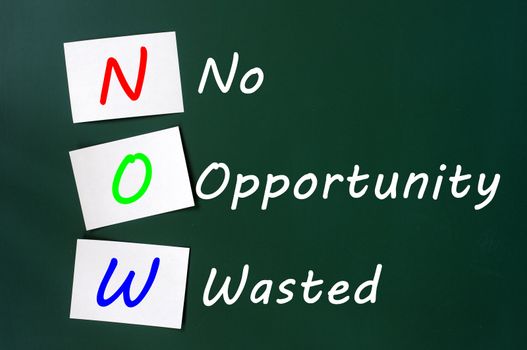 Acronym of NOW - No Opportunity Wasted written on a green chalkboard with sticky notes 