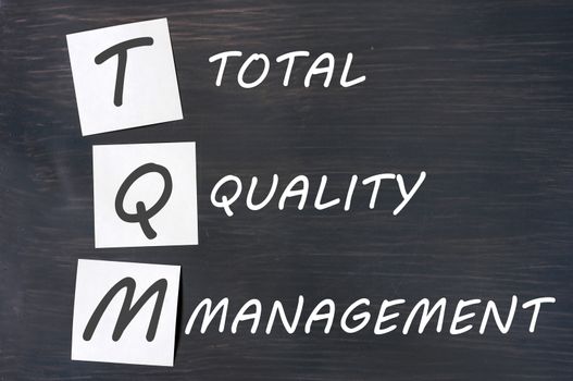 Acronym of TQM for total quality management - white chalk handwriting and sticky notes on a blackboard 