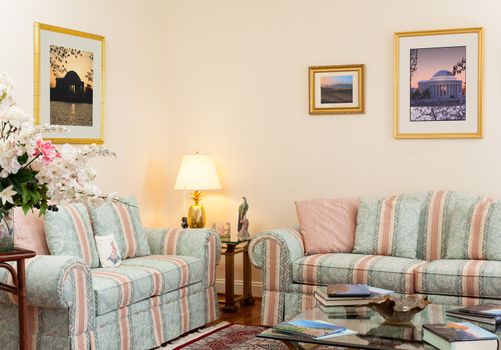 Modern living room with green and pink settees, glass table, books and prints on wall