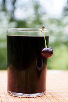 Glass of natural fresh cherry juice on a table in a summer garden