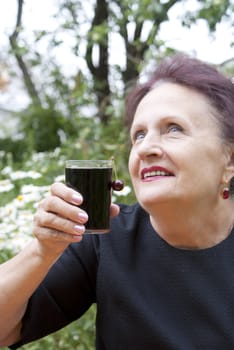 The happy smiling woman drinks fresh cherry juice