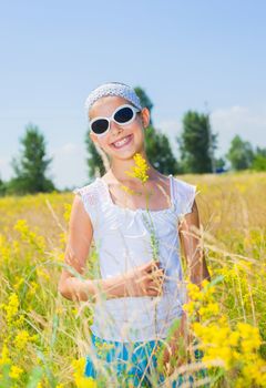 Adorable girl in glasses with flowers in yellow field. Summer freedom andjoy concept. Vertical view