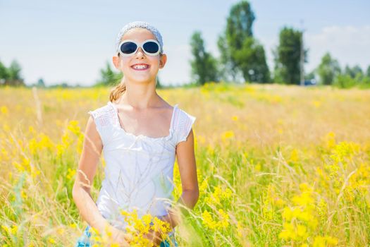 Adorable girl in glasses with flowers in yellow field. Summer freedom andjoy concept.