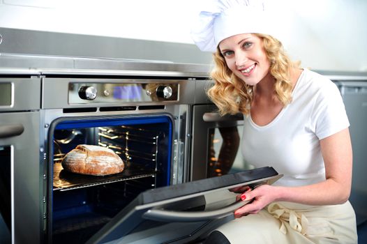 Pretty baker opening an oven door. Ready to pull out baked bread