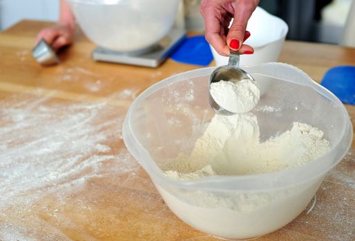 Female hand collecting flour from bowl in spoon. Closeup shot