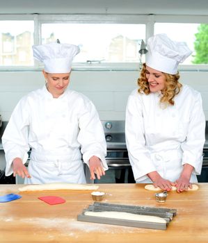 Senior chef teaching newbie female chef, how to roll and knead dough