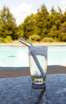 Plain glass of water with ice cubes on side of blue swimming pool