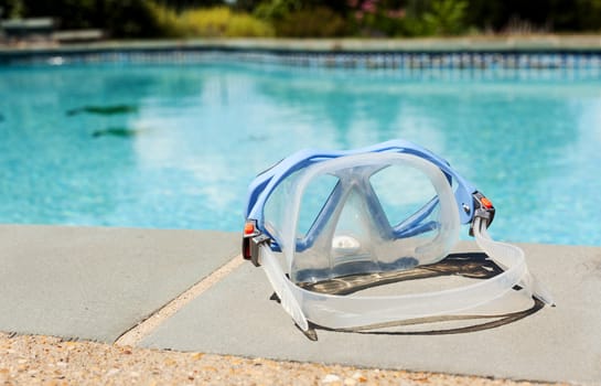 Silicone swimming mask sitting on edge of blue swimming pool in summer