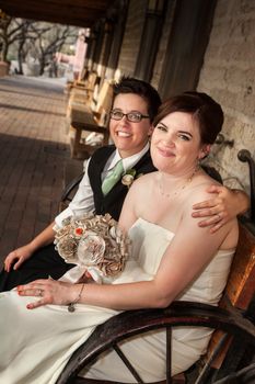 Caucasian lesbian newlyweds sitting on rustic bench