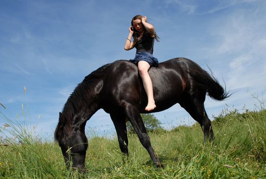 young woman and her black stallion in a field in spring