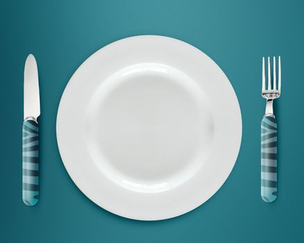 empty white plate with knife and fork on blue background.