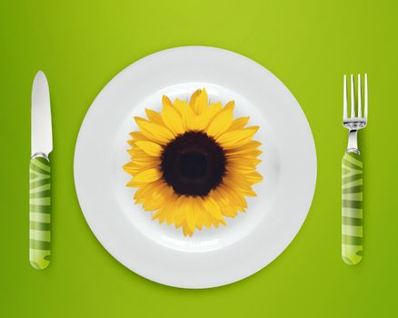 sunflower on white plate with knife and fork on blue background.