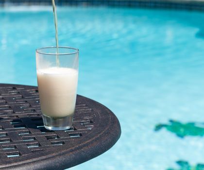 Plain pint glass of beer being poured sitting on table by blue swimming pool