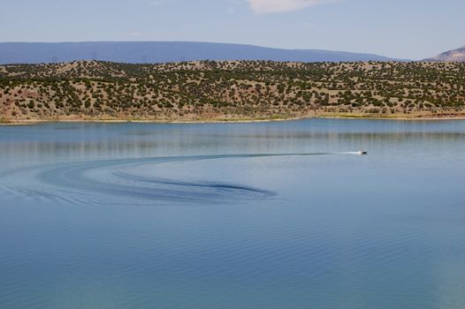 Speedboat leaving a trail in it's wake on a large lake with mountains and blue sky in the background, with copy space.