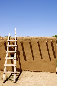 New Mexican Adobe Pueblo Building, featuring a ladder and shadows, on a native American Indian reservation (outside Taos), against a deep blue sky with copy space.