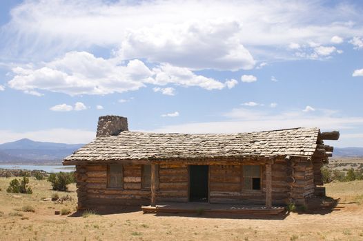 Rustic 'wild west' log cabin, against blue sky, with mountains and desert, with copy space.