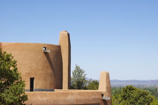 New Mexico curved Adobe Building with a backdrop looking out over Santa Fe, against a blue sky with copy space.