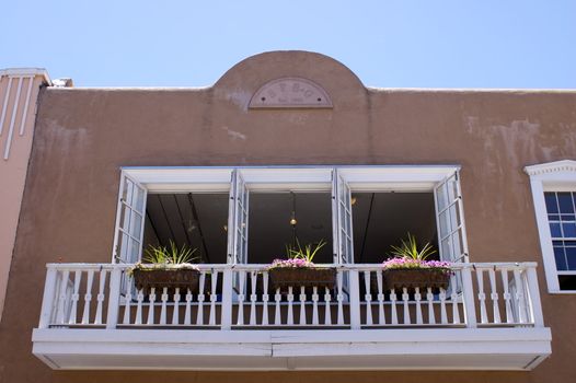 Looking up at a New Mexican Adobe Building , featuring a characterful triple white window with pretty balcony, against a blue sky with copy space.