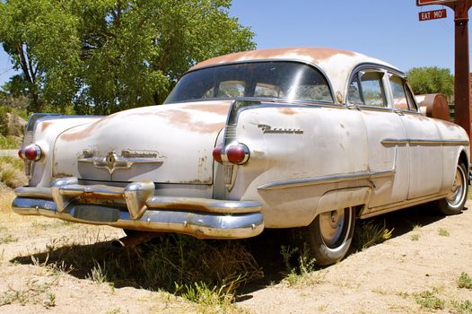 Rusting vintage American car (Packard), taken along the side from the back, parked outdoors.