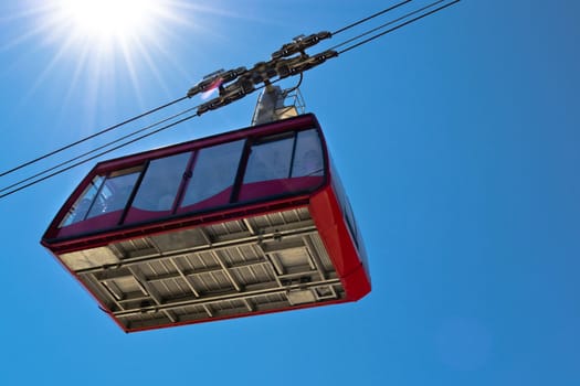 Ropeway wagon moving to the mountain peak with blue sky on background
