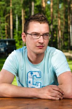 Young and attractive man in glasses outdoors portrait with forest on background