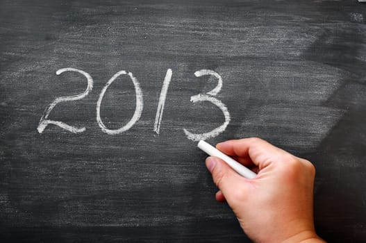 2013 written in chalk on a smudged blackboard,with a hand holding chalk