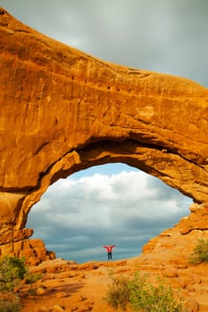 Woman staying with raised hands inside an Arch in the Arches National Park, UT