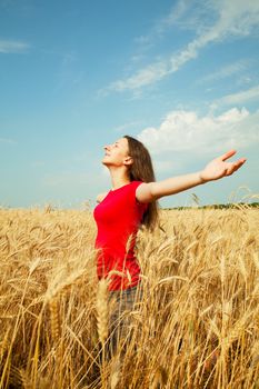 Teen girl staying at a wheat field with her arms outstretched
