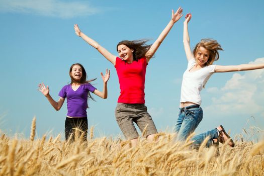 Teen girls jumping at a wheat field in a sunny day