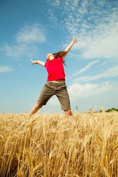 Teen girl jumping at a wheat field in a sunny day