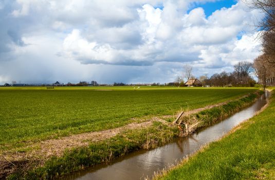 Dutch farmhouse close to river and with nice sky with many clouds