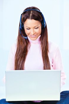 Pretty young woman with headphones looking at laptop at home