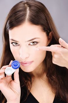 Young woman holding contact lenses cases and lens in front of her face